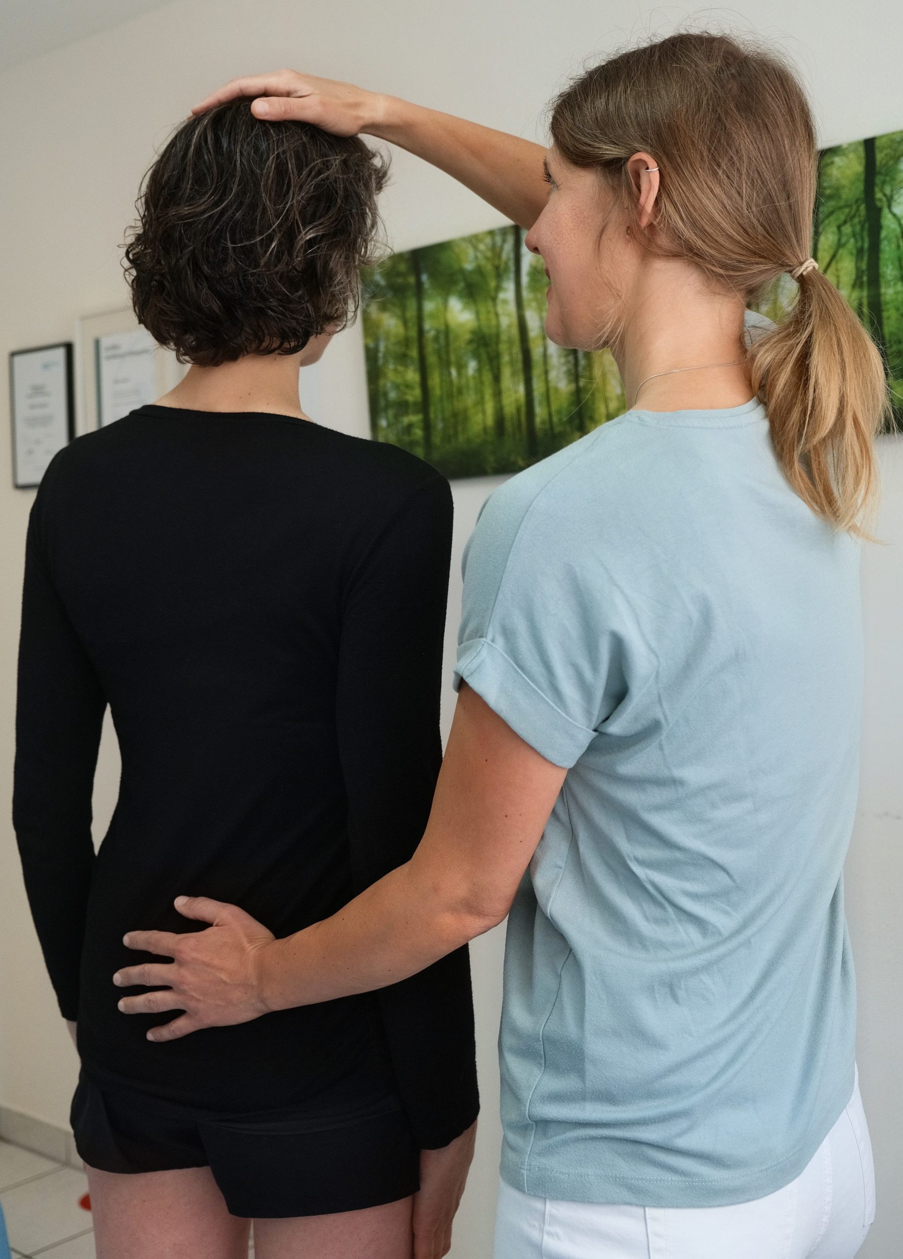 Stehende Patientin, Hände der Therapeutin auf dem Kopf und dem Kreuzbein.